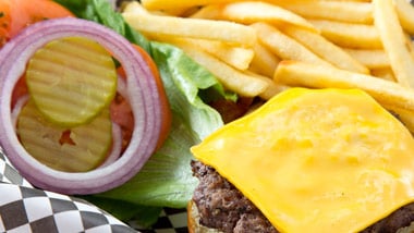 burger with cheese, lettuce, tomato, onion and pickle in a basket with fries