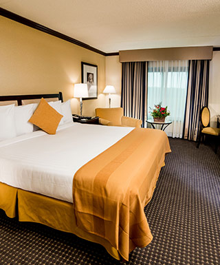 king bed in hotel room with tan bedspread and white sheet