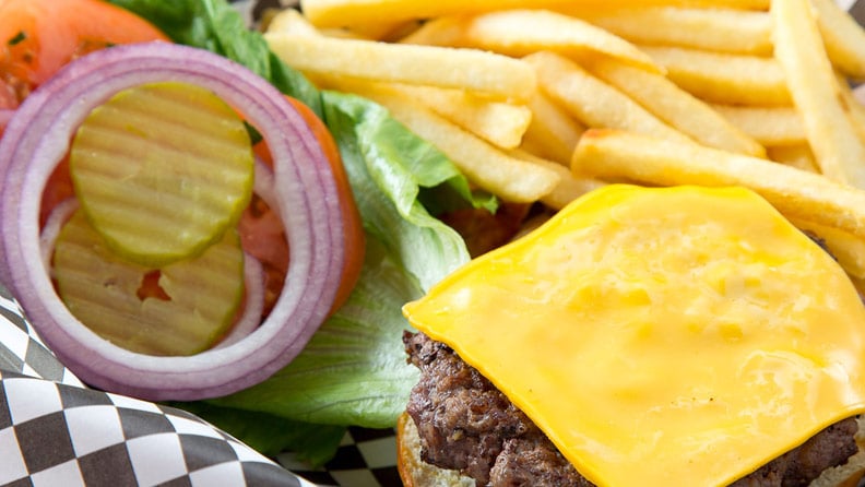 burger with cheese, lettuce, tomato, onion and pickle in a basket with fries